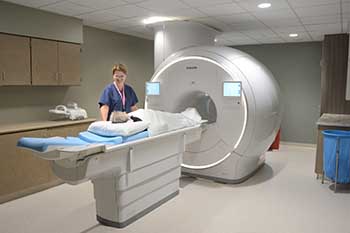 Elder woman being slid into CT scan machine by reassuring female imaging technician